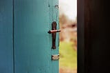 blue door opening up slightly to blurred background of outside