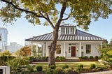 A small white house with a yard and tree in front.