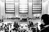 Woman on foreground looking at Grand Central Station’s main foyer in background. Black and white.