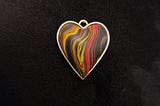 Picture of a coloured heart with black, red, yellow and orange swirls on black background.