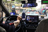 Chofe er interior de un auto con varios dispositivos conectados: 2 celulares, GPS, monitor del auto, taximetro