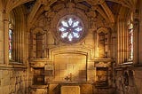 An old stone building with a star-shaped window and an altar on which a small cross is placed.