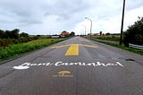 Road in rural area with a giant yellow arrow pointing forward and the words Bom Caminho