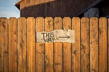 A rustic fence made of brown wood holds a sign that says “THIS WAY” with an arrow pointing to the right.