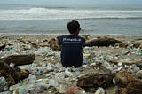 Picture of a man sitting on a plastic strewn beach, facing the ocean