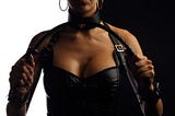 Woman dominatrix wearing black leather corset and holding a whip.