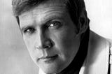 A black-and-white publicity head shot of Lee Majors from 1973 — The Six Million Dollar Man era. He is wearing a turtleneck sweater and a light-colored jacket with a large lapel.