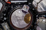 The Moon Gallery, 64 small artworks in a specially built grid box, floating in microgravity aboard the International Space Station with a view of the earth behind it.