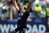 a cricket player celebrates on his knees and looks upward after taking a wicket in a match.