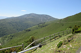 A broken fence guarding a steep hillside; green hills on the horizon