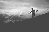 silhouette of man balancing on sloped hillside with cloudy sky in background