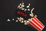 A mobile screen is displaying Netflix and popcorn is spilled around the device.