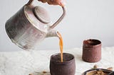 Person pouring a hot coffee-like liquid into handless mugs.