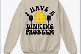 White sweatshirt reading “I have a dinking problem” with an image of a pickleball and paddles.