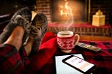 Slippered feet resting on a table next to hot tea in front of a fire