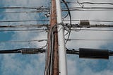 A telephone pole with a dozen wires running from either side of it, viewed upward from the base of the pole.