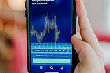 Person holding a smartphone with a cryptocurrency graph displayed on the screen