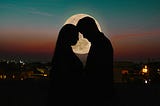 A silhouette of a couple with a view of a full moon.