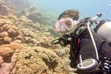 Image of a girl scuba diving with corals in the background