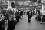 Black and white panoramic, lower than eye-height view photograph of people in St. Pancras station, London
