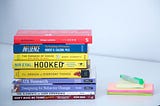Vários livros de design empilhados, ao lado dos livros alguns post-its coloridos e uma caneta marcadora na cor verde.