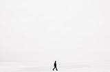 A dark silhouette walking through a vast empty white space.