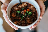 delicious and hearty beef stew served in a white bowl, showcasing tender chunks of beef, colorful vegetables, and a rich brown broth.