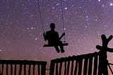 Silhouette of a person in a swing against a starry evening sky