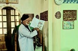 Domullo Shermuhamad stands at the front of the mosque reading from a Healthy Mother, Healthy Baby booklet.