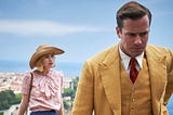 A screenshot from the 2020 film Rebecca. Lily James stands in the background Armie Hammer stands in the foreground.