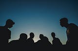 Silhouette of a group of people sat together (https://unsplash.com/@papaioannou_kostas)