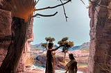 A photo of a diorama of Jesus being baptized by John. Stone cliffs are on either side; Jesus is standing in a stream. John is on the bank, with his hand reached out over Jesus.