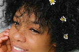 A Black girl with flowers in her hair smiles.