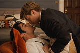 Two men — one blond, one brunet — kiss.