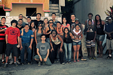 Grupo de mais de 20 pessoas posando para foto na calçada em frente à casa.