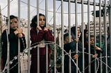 Palestinian women & children peer through the bars of yet another randomly constructed Israeli choke point in Hebron