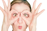 Close-up of woman’s face as she makes imaginary glasses over her eyes with her thumbs and forefingers.