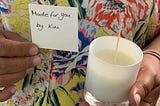 A woman holds up a newly-made candle with a note that says “Made for you by Kim.”