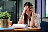 A stressed young woman holds her head while looking at financial information.