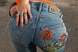 A woman wearing patchwork jeans, humorously sticking her butt out to the camera