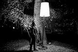 A man stares up at a lamp in the wilderness
