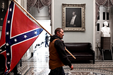 A man stands in the capital holding a confederate flag.