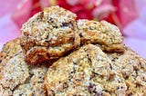 Scones flecked with chocolate and sanding sugar, stacked with a soft white background with blurred red and gold ribbon and pink and red flowers. Inspired by Lady Danbury