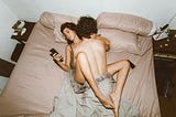 A couple is intimate with one another while the female uses a smartphone.