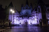 A nighttime photograph of the Royal Courts of Justice in London, UK