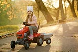 Girl riding a plastic tractor on a path in Autumn