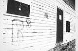 black and white photograph of the side of a building with hand-painted blinds and the letter RS spray painted on the siding