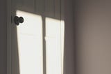 An image of sunshine casting shadows across a closed white door with black door knob.