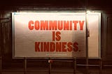 Billboard with a white background and red writing saying, “Community is Kindness”