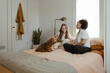 two women and a dog sitting on a bed